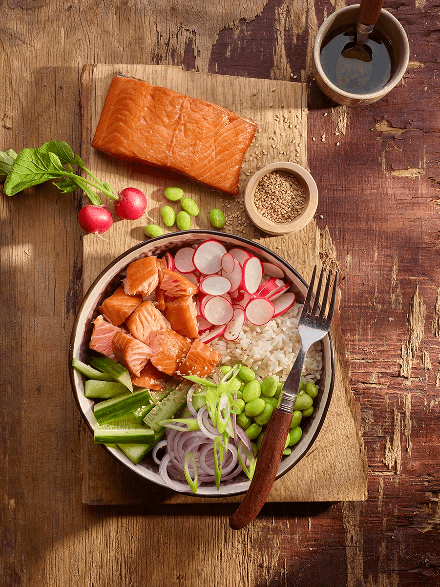 Bol de poke au saumon et légumes frais sur fond de bois rustique.