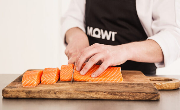 Un cuisinier coupe du saumon en darnes sur une planche en bois.