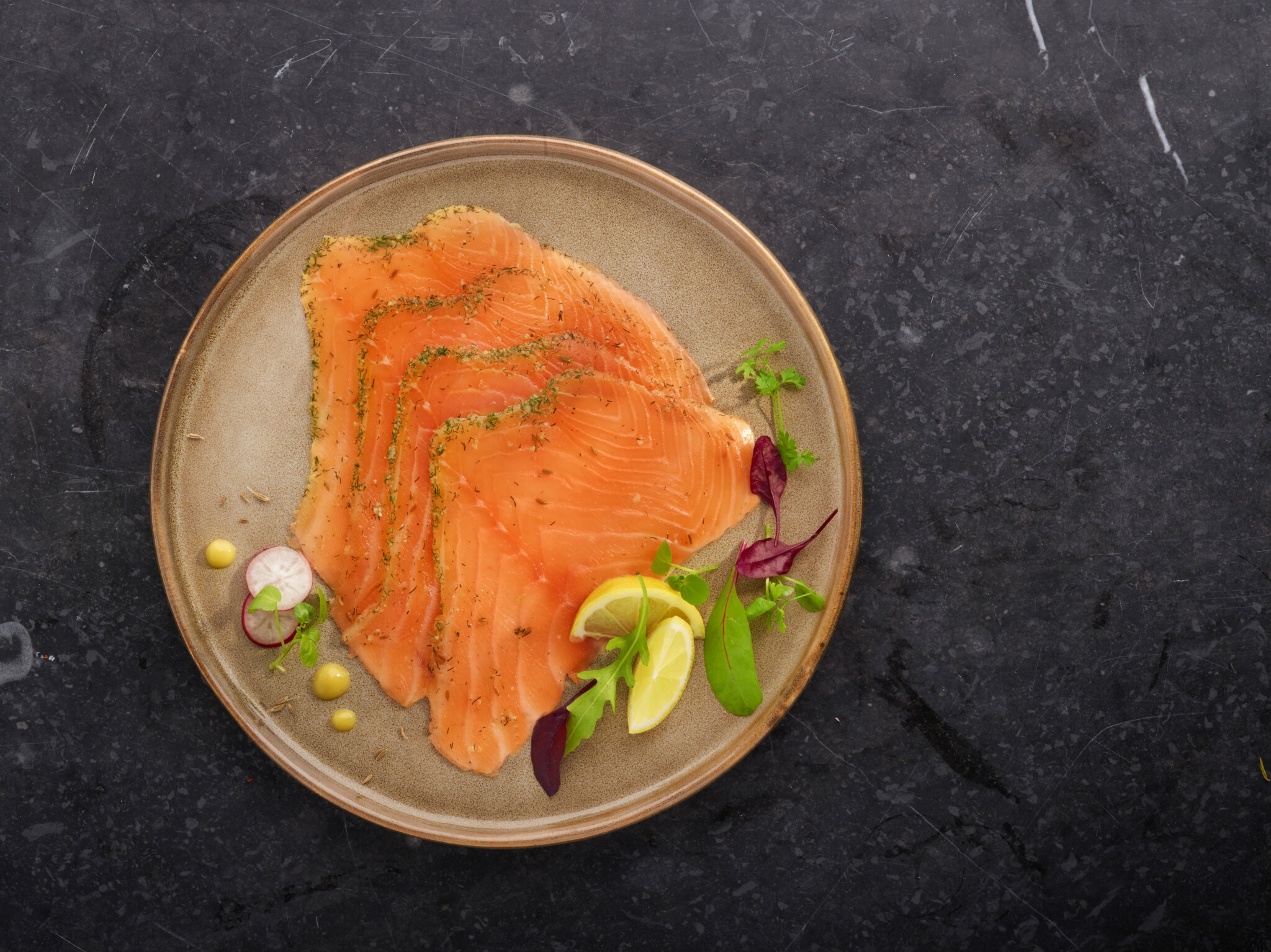 Tranches de saumon fumé sur une assiette garnie de citron, radis et herbes.