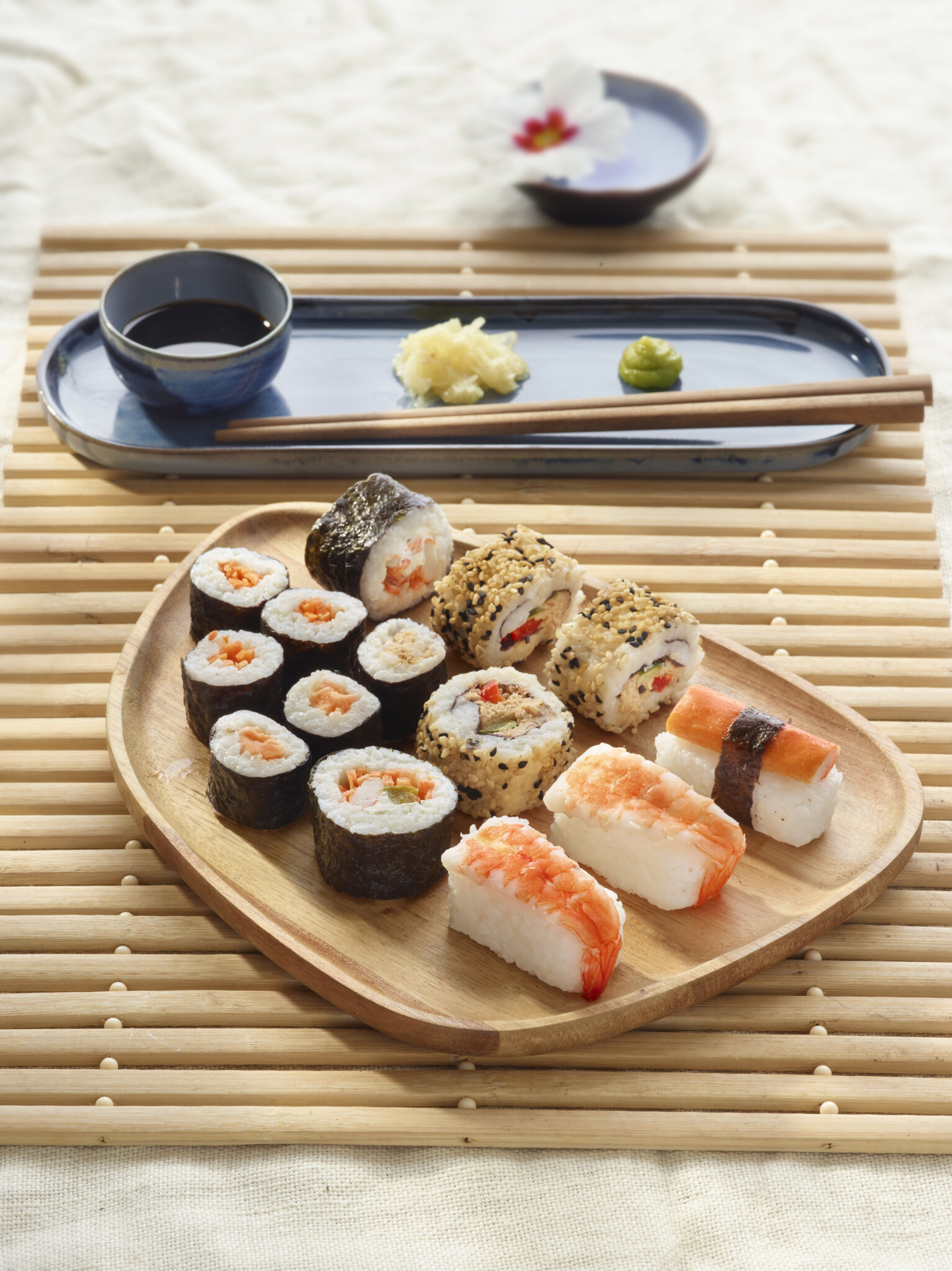 Assortiment de sushis variés sur une assiette en bois, avec sauce soja, gingembre et wasabi.