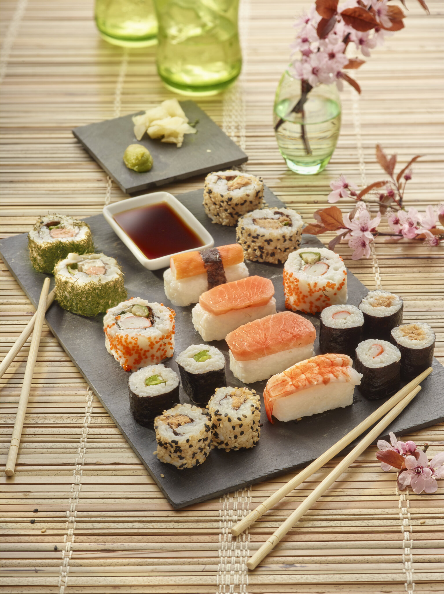 Assortiment de makis et sushis variés, avec des accompagnements et des fleurs de cerisier en arrière-plan.