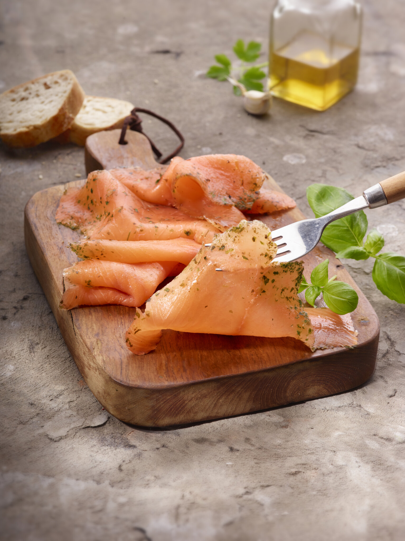 Saumon fumé tranché sur planche en bois avec des herbes et une fourchette.
