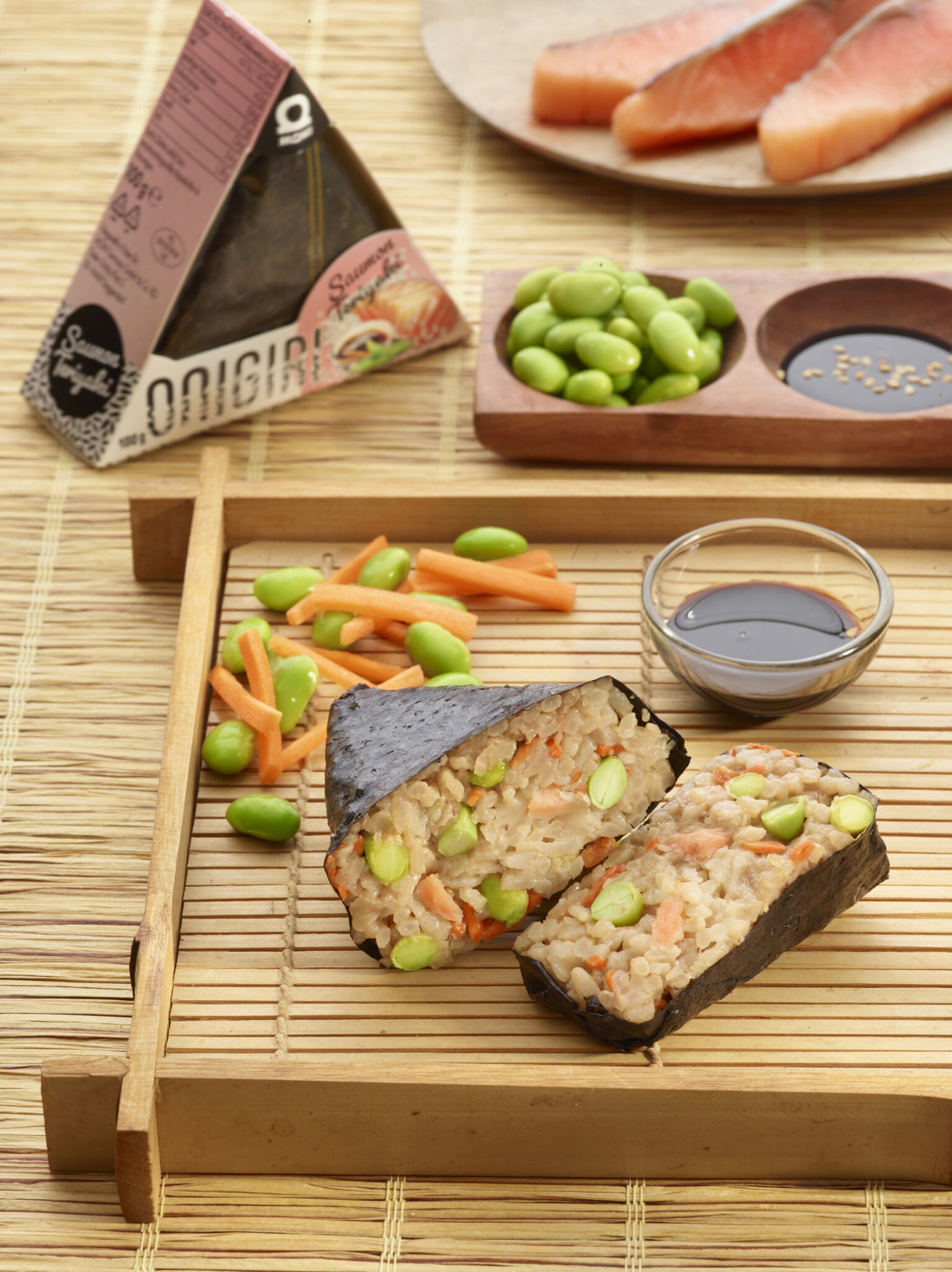 Onigiri au saumon teriyaki avec edamame et carottes sur un plateau en bambou.