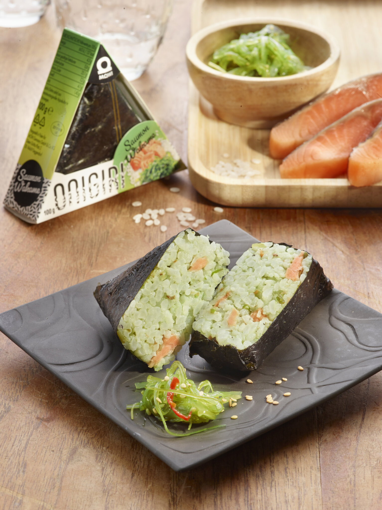 Onigiri triangulaires au saumon et wakame sur une assiette avec un bol de wakame et du saumon cru.
