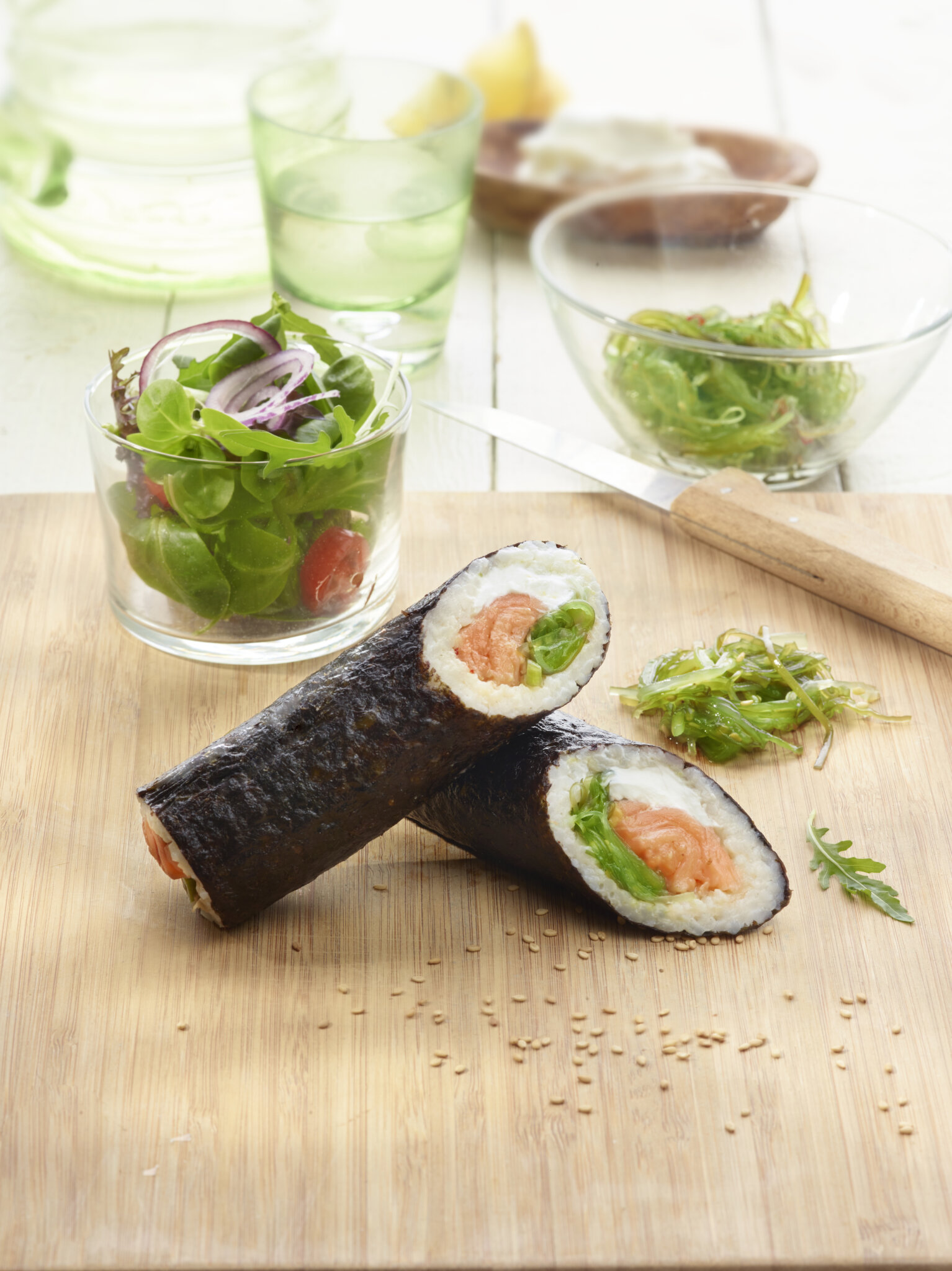 Deux makis au saumon et leurs accompagnements sur une planche en bois.
